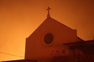 A church in Pacific Palisades, Los Angeles, cast in a horrid glow of the oncoming firestorm hunting it down for devouring (Public Domain).